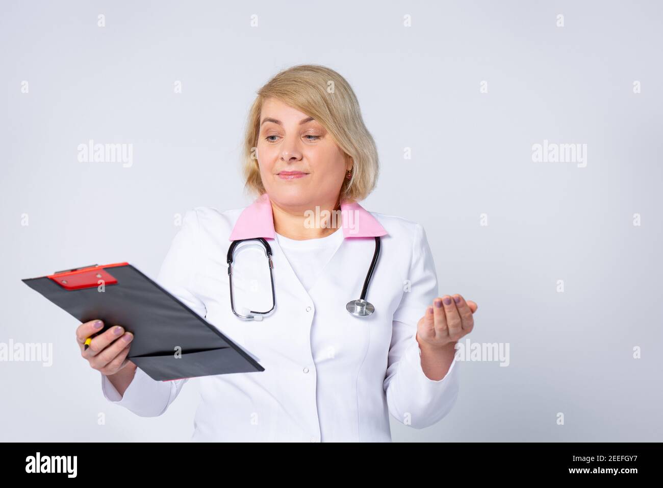 Médecin de haut niveau, femme aux cheveux blonds, portant un uniforme médical, regardant sur un dossier de feuilles avec ordonnance. Expression confuse avec les bras et Banque D'Images