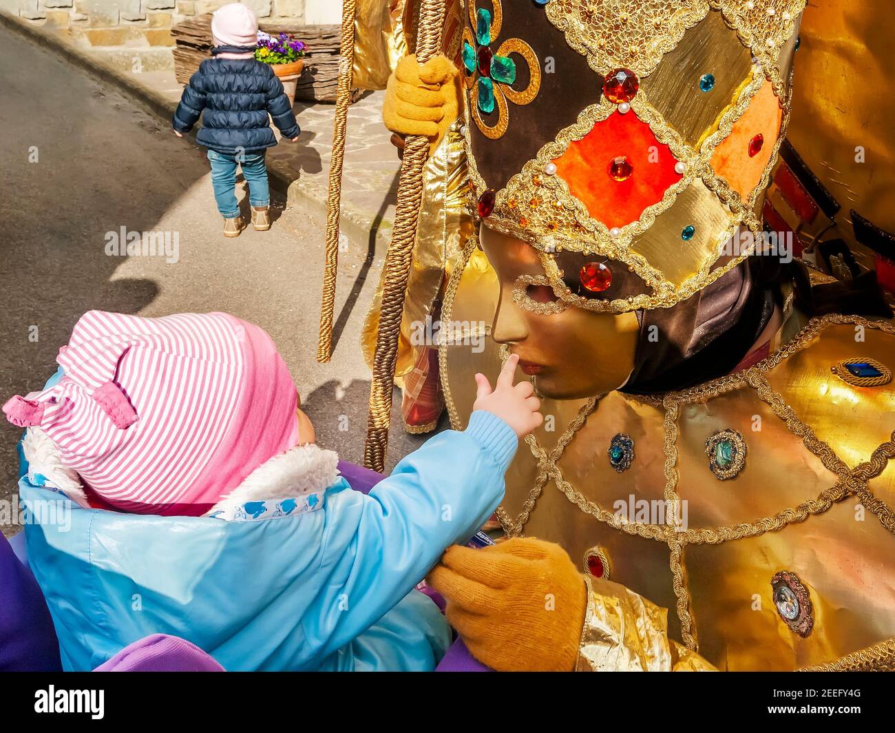 Un petit enfant caresse un beau et coloré carnaval traditionnel masque en plaçant son doigt sur son visage Banque D'Images