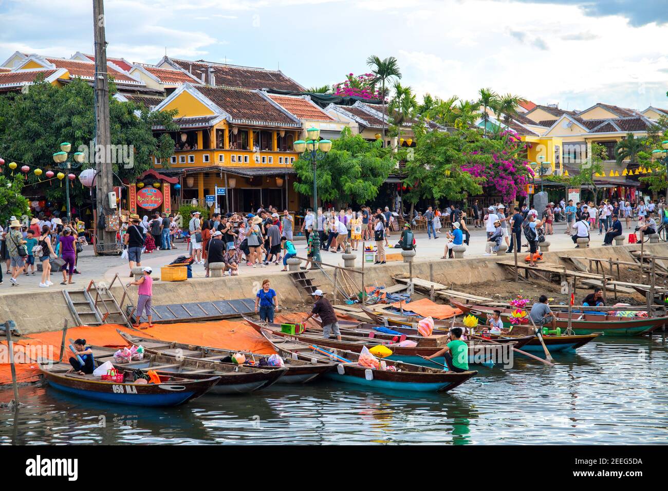 Hoi an, Vietnam - 27 juillet 2019 : ville historique au bord de la rivière avec des bâtiments jaunes et des touristes. Les gens affluent sur les remblais. Bateau traditionnel en bois à VI Banque D'Images