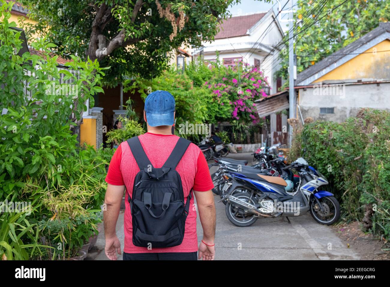 Homme avec des promenades à dos dans la rue verte de la ville tropicale asiatique. Les jeunes routards voyagent au Vietnam. Petit paysage de ville asiatique. Touriste européen à Ho Banque D'Images