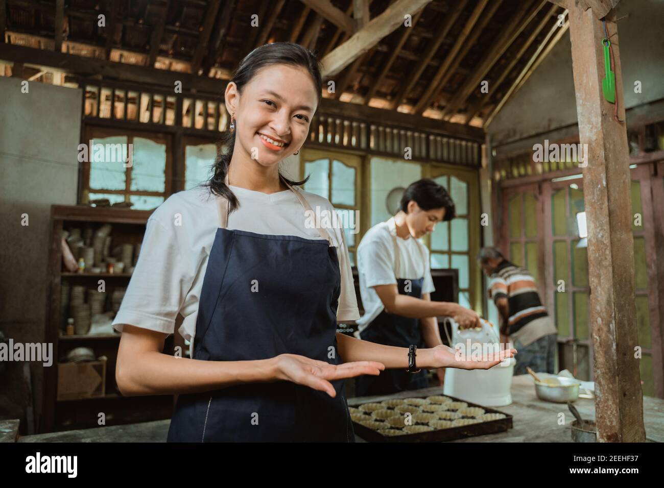 Belle employée en tablier vous offrant quelque chose de ses paumes sur le fond de la cuisine Banque D'Images