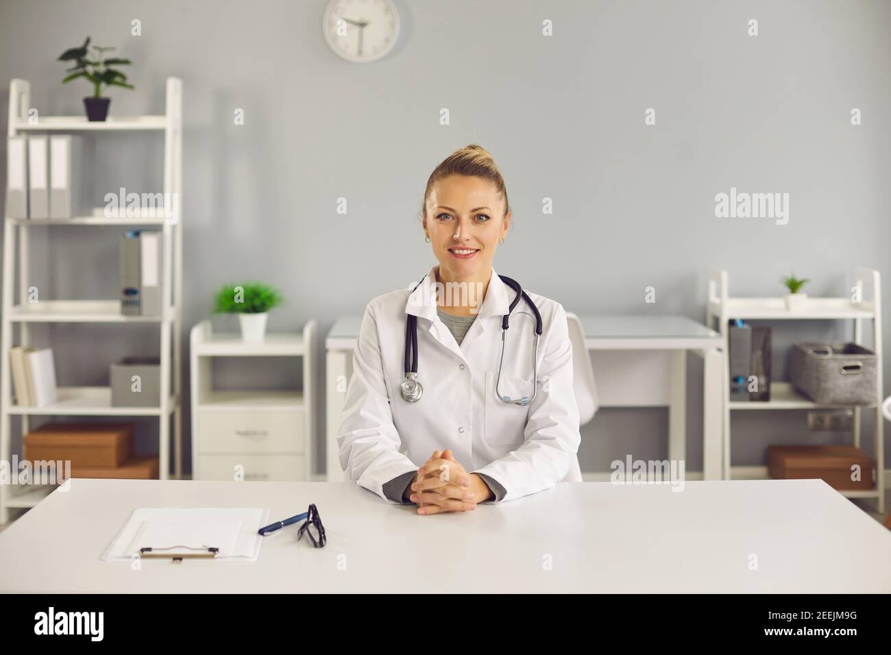 Sympathique jeune médecin souriant assis à son bureau à la clinique ou à l'hôpital Banque D'Images