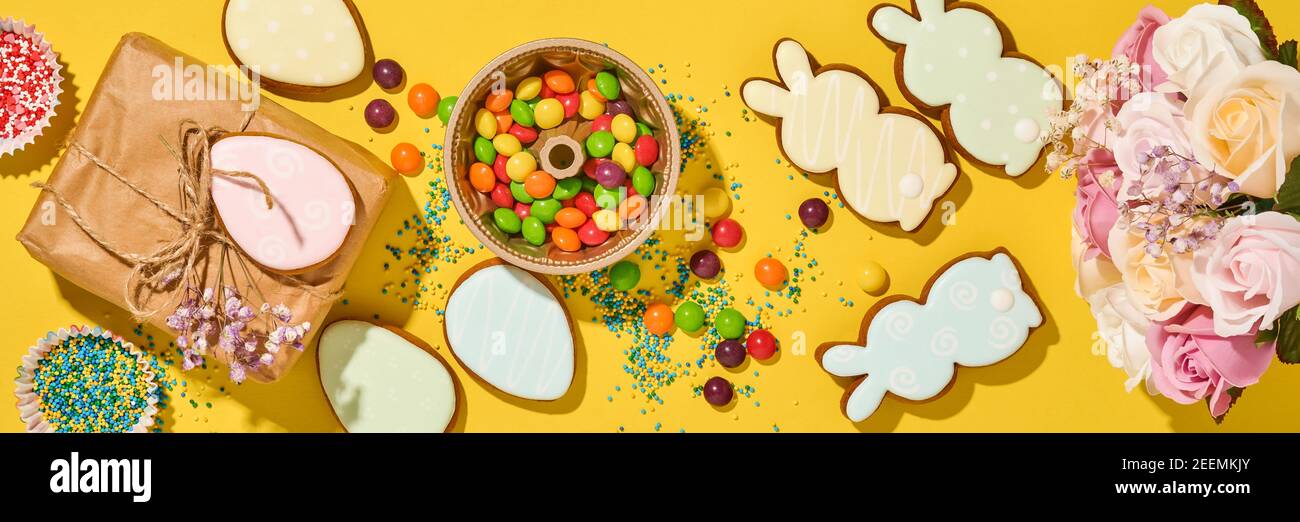 Fond de cuisson de Pâques. Pain d'épice multicolore de Pâques, bonbons, vinaigrette aux confiseries éparpillées et boîte cadeau sur fond jaune. Célèbre Banque D'Images