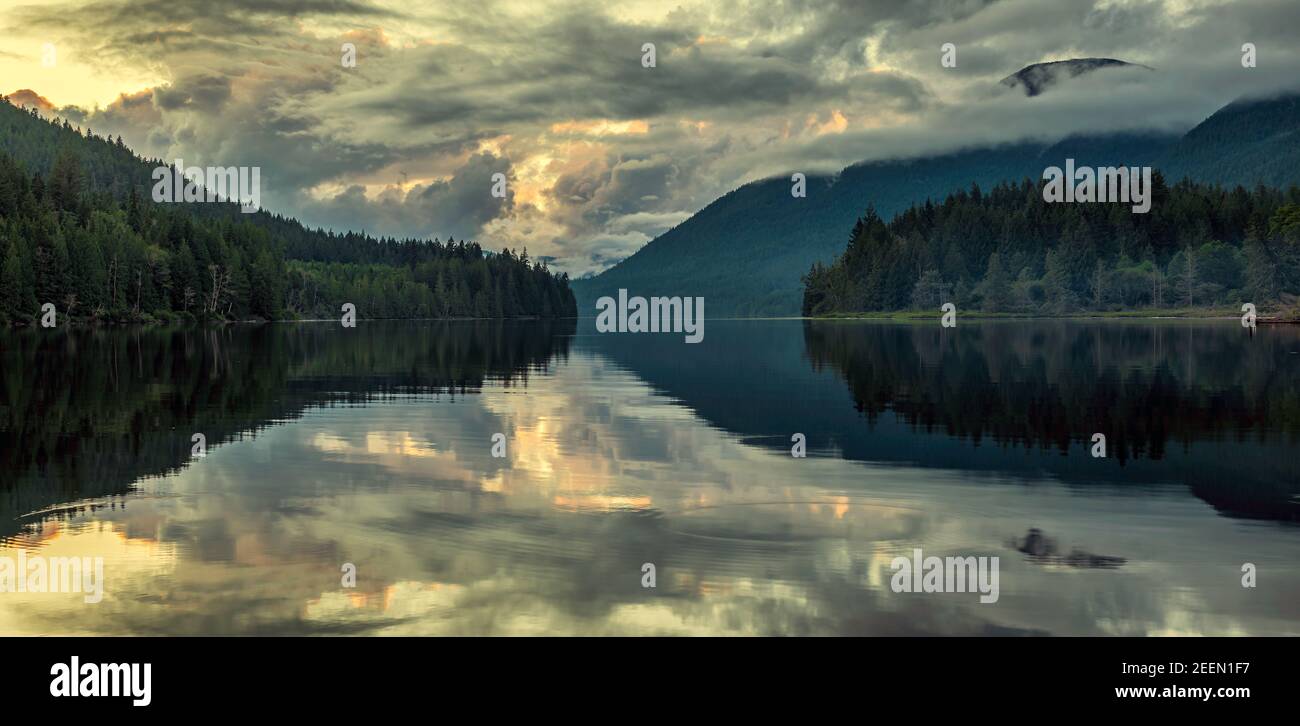 Des nuages spectaculaires au-dessus d'un lac fixe avec réflexion et arbres à distance. Banque D'Images Des nuages spectaculaires au-dessus d'un lac fixe avec réflexion et arbres à distance. Banque D'Images