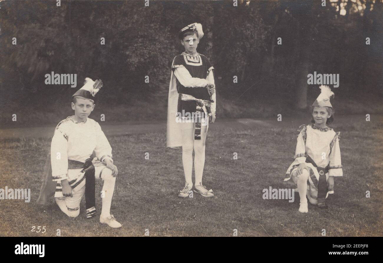 Carte postale photographique vintage du début du XXe siècle montrant trois enfants en plein air portant une robe de théâtre. Banque D'Images