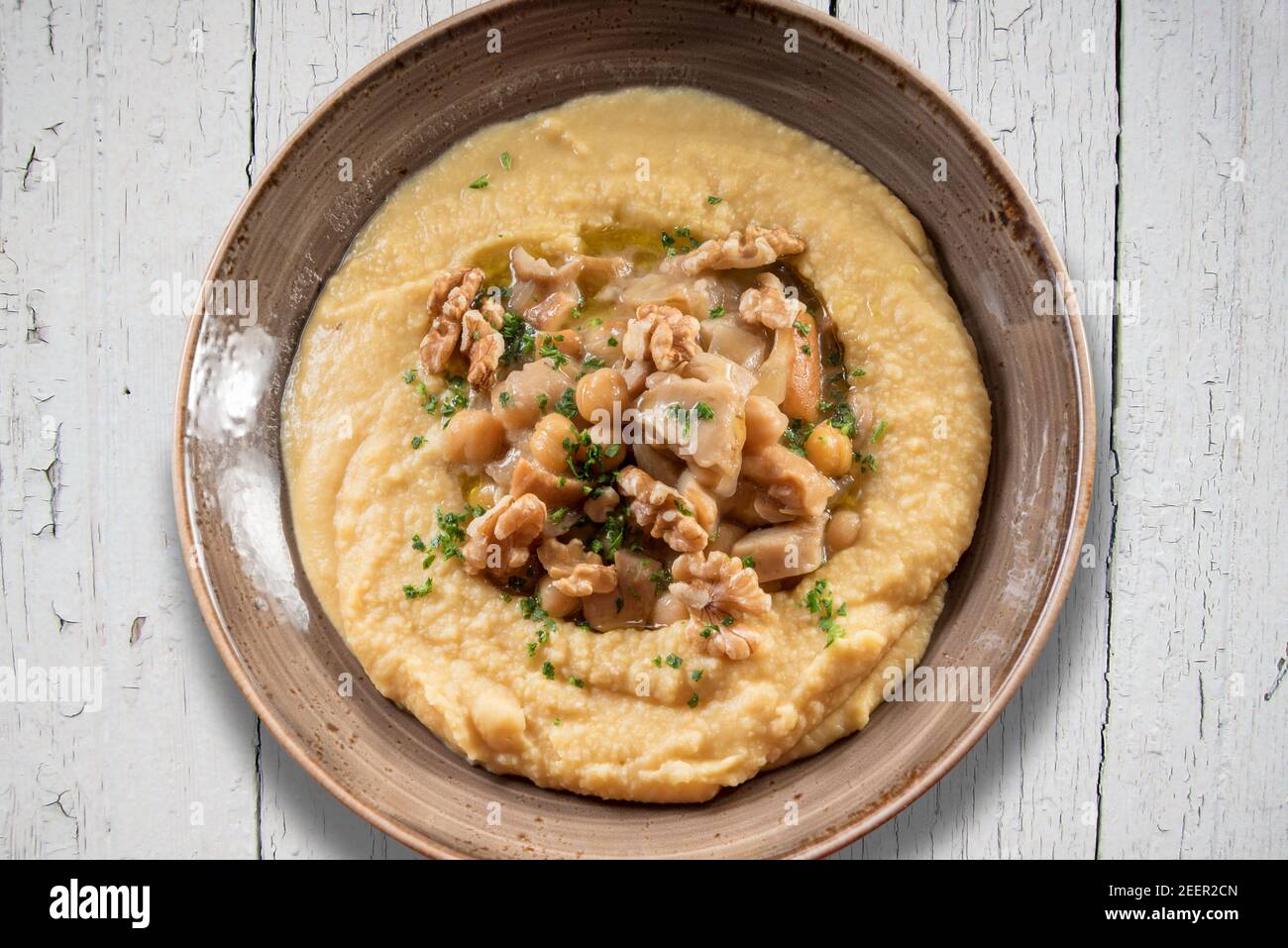 Houmous au persil, à l'huile d'olive et aux noix. Crème israélienne de pois chiches en faïence, bol sur table rustique, vue de dessus, plat Banque D'Images