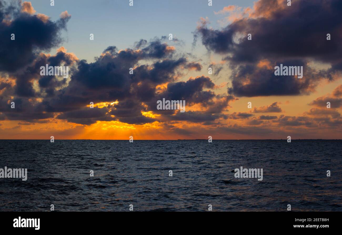 Des faisceaux de lumière orange éclairent à travers des nuages spectaculaires sur le bleu La mer du nord de l'Allemagne au coucher du soleil Banque D'Images