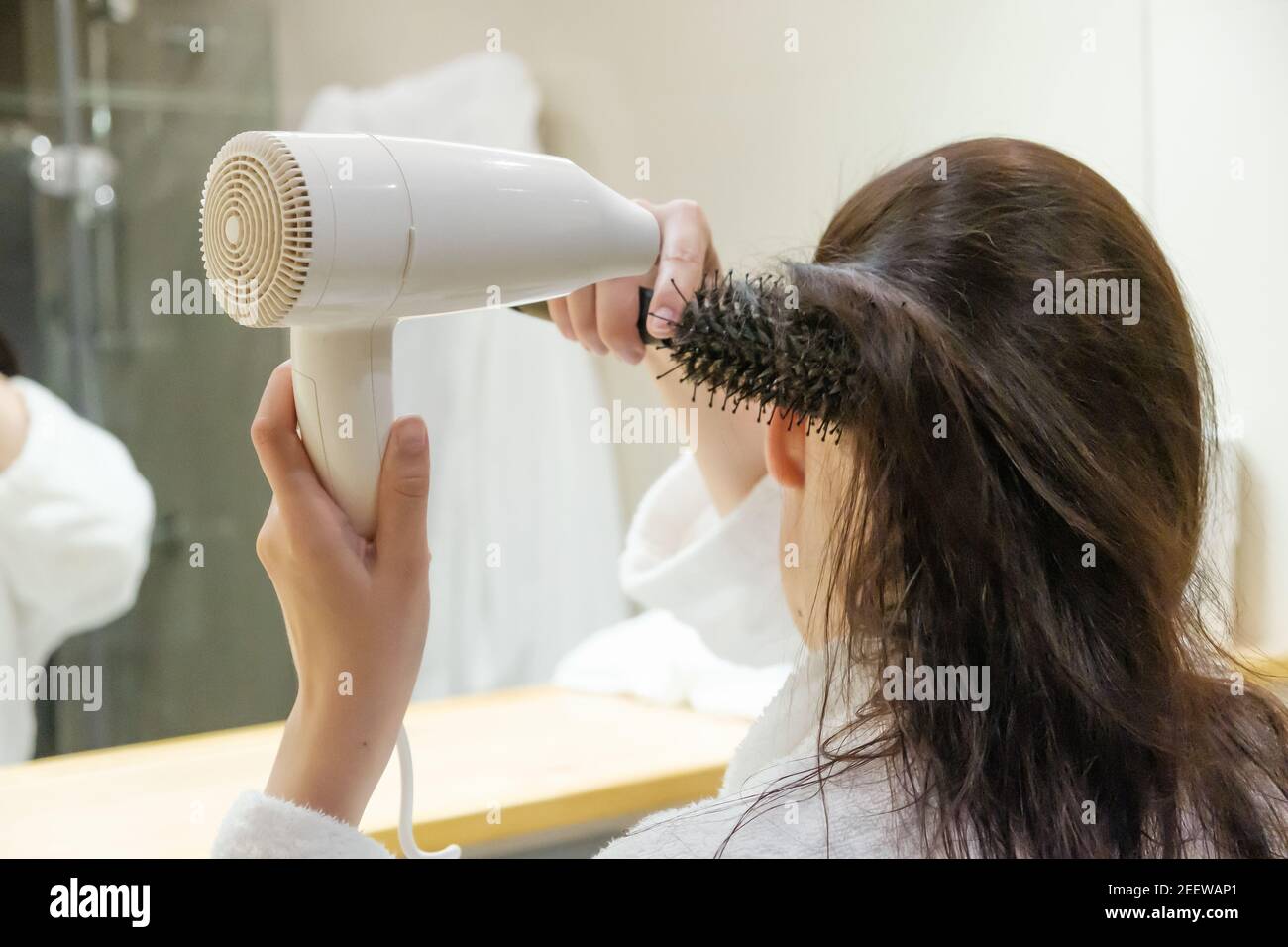 Jeune femme séchant les cheveux avec un sèche-cheveux et coiffant les  cheveux avec une brosse ronde dans la salle de bains. Routine du matin  Photo Stock - Alamy