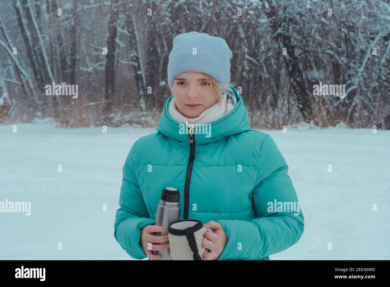 une jeune fille de 15 ans qui marche dans la forêt hivernale contient des thermos et une tasse de thé chaud. Pique-nique dans la neige. Banque D'Images