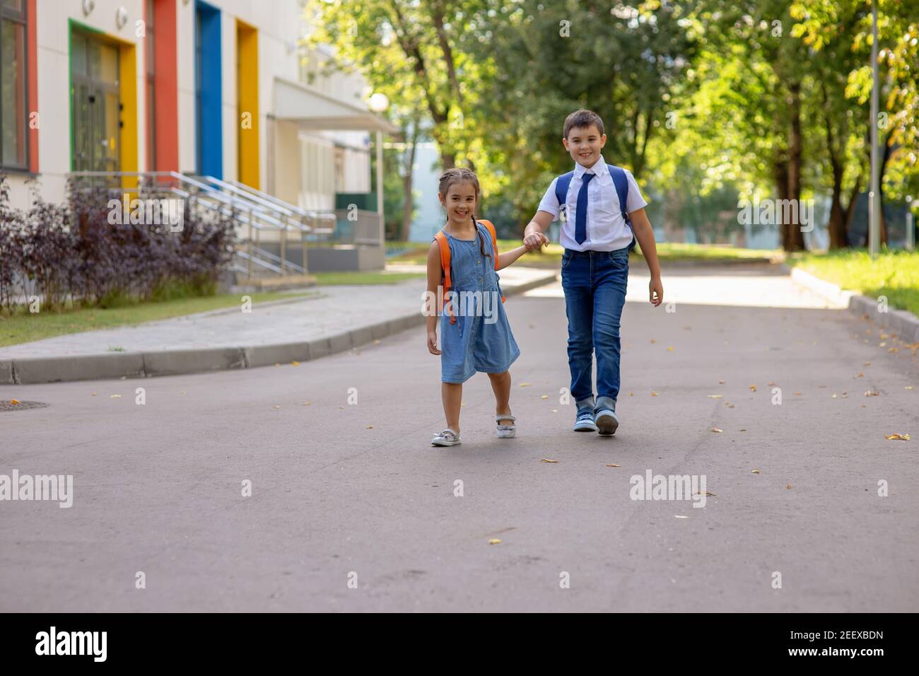 Les écoliers gaies, une fille et un garçon dans une chemise blanche avec des sacs à dos, vont de l'école. Banque D'Images