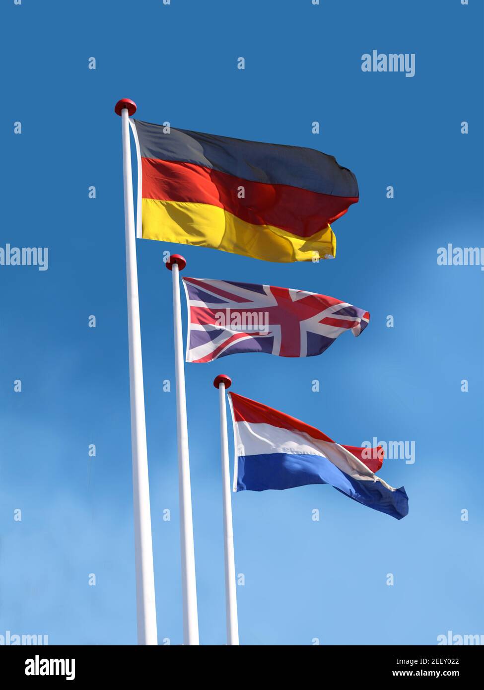 Drapeaux de l'Allemagne, du Royaume-Uni et de la France sur les mâts de drapeaux. Le drapeau de l'Allemagne est en haut. Fond bleu ciel. Banque D'Images