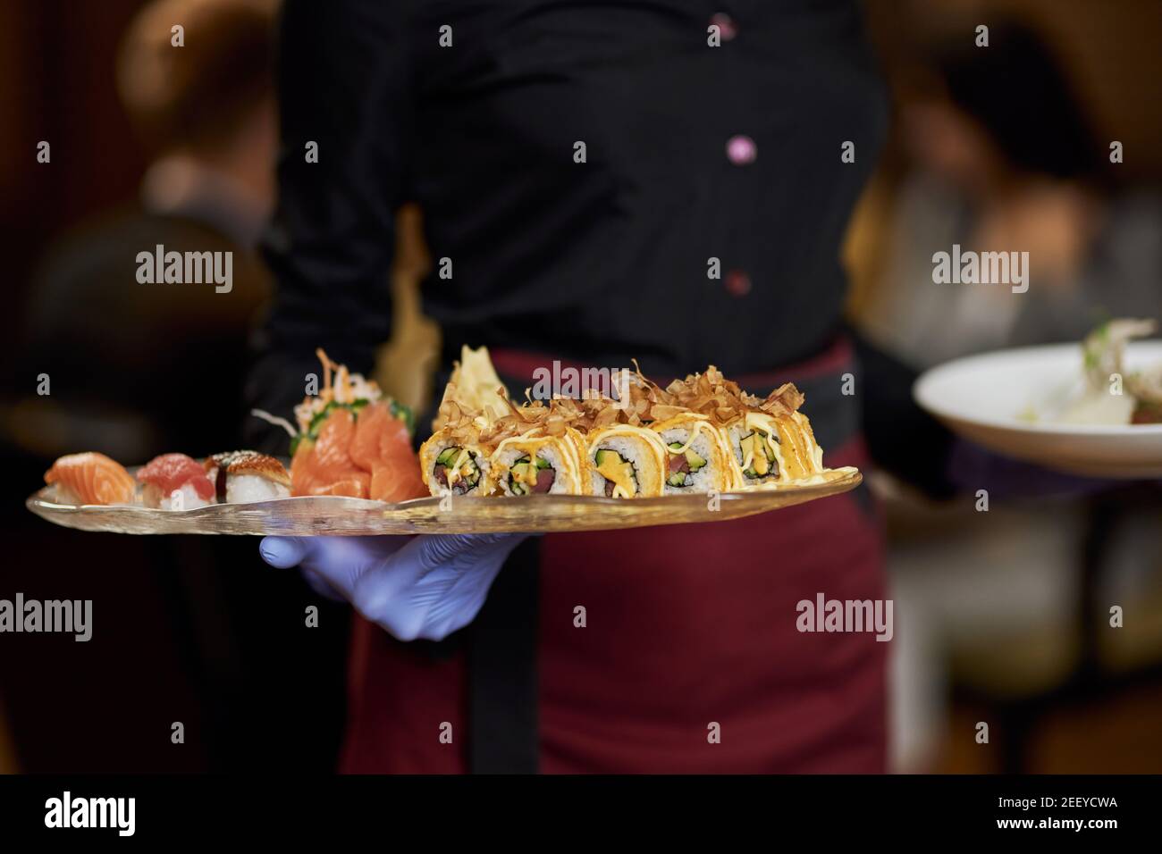 Photo rognée d'une serveuse dans des gants en caoutchouc tenant une assiette avec de délicieux sushis Banque D'Images