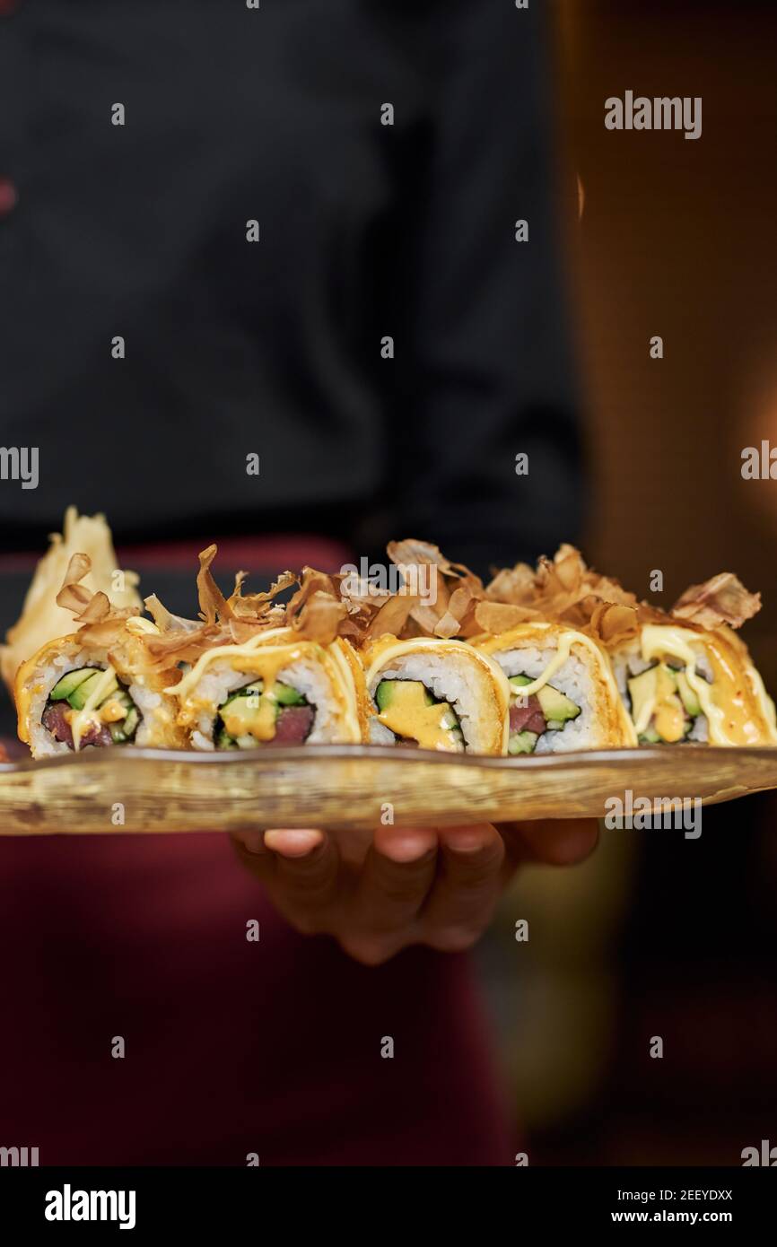 Photo rognée d'un serveur qualifié tenant une assiette avec savoureux sushi avec avocat Banque D'Images