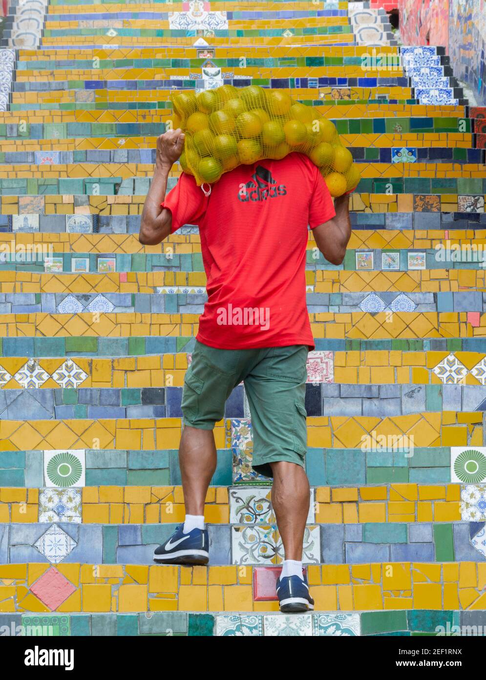 RIO DE JANEIRO, BRÉSIL - 3 JANVIER 2020 : un ouvrier porte un sac d'oranges en début de matinée sur la célèbre Escadaria Selaron (escalier de Sélaron) Banque D'Images