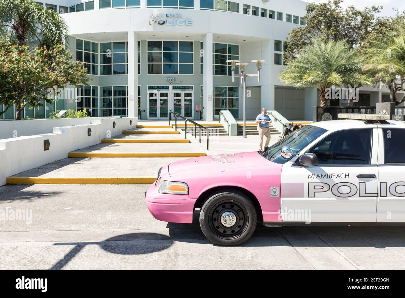 Un homme marche à côté d'une voiture de police désaffectée de Miami Beach peinte en rose à l'extérieur du service de police de Miami Beach. Banque D'Images
