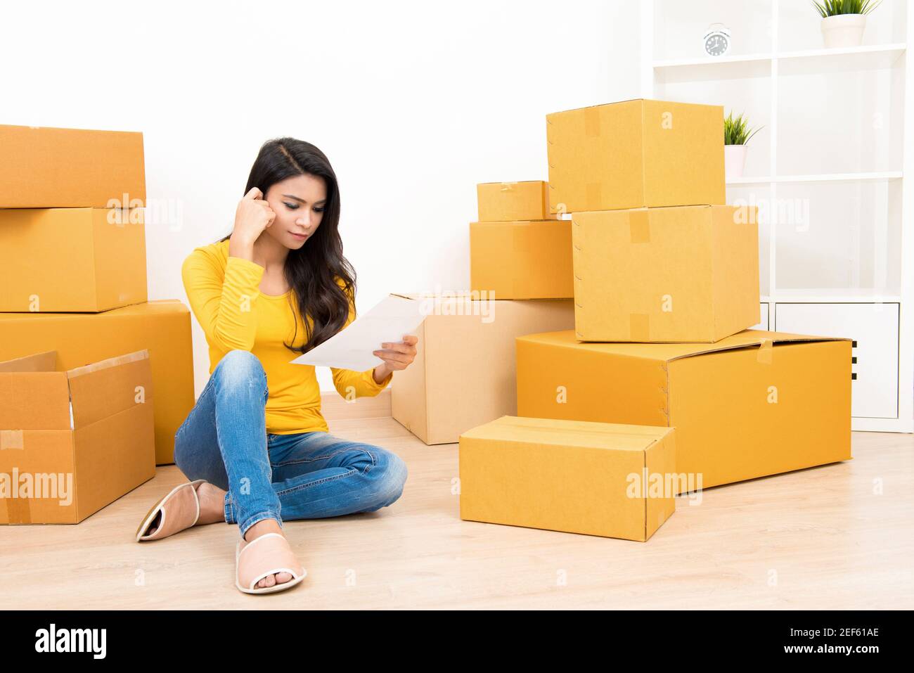 Jeune femme asiatique assis avec des boîtes sur le sol - passer au nouveau concept de maison Banque D'Images