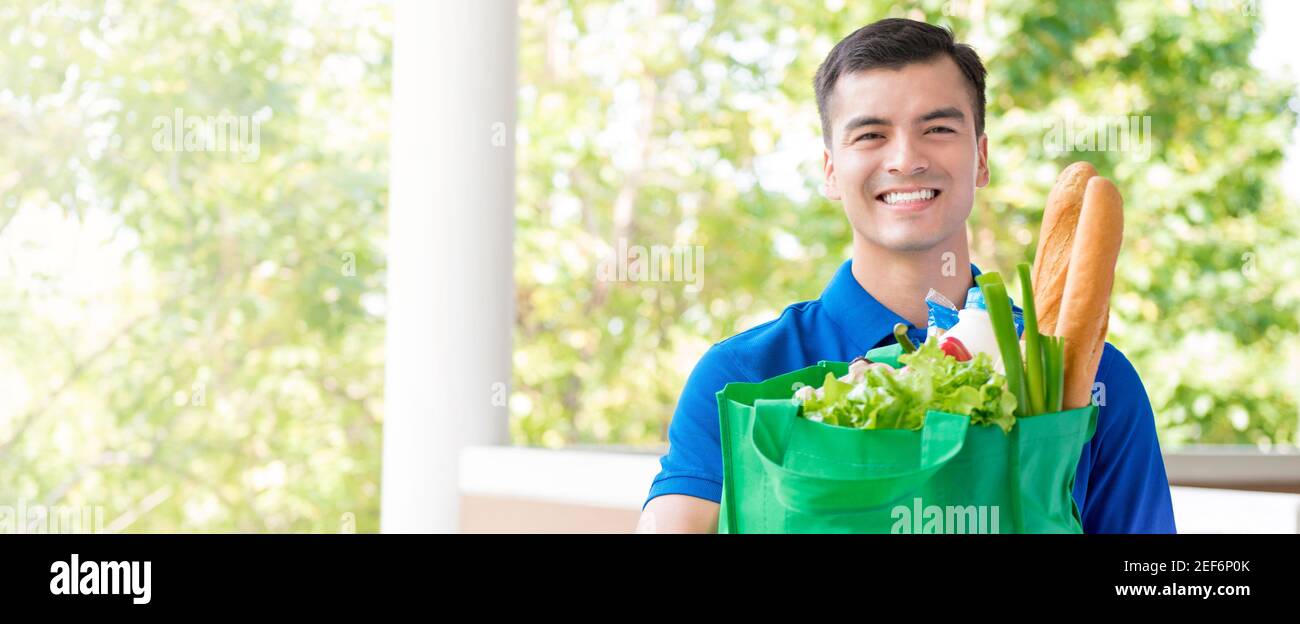 Un liveur souriant tient le sac de recyclage de l'épicerie avec la nourriture intérieur - bannière panoramique Banque D'Images