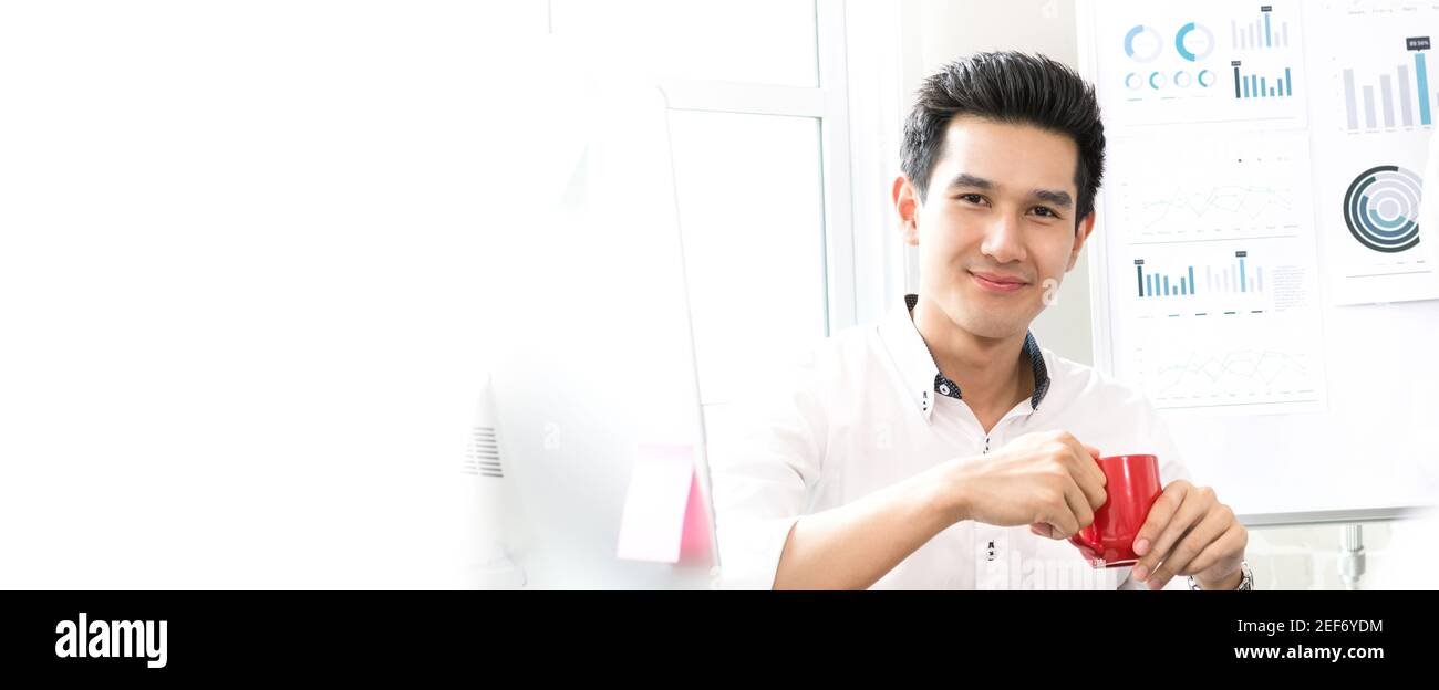 Beau homme d'affaires asiatique décontracté souriant tout en tenant une tasse de café au travail, bannière panoramique avec espace de copie Banque D'Images