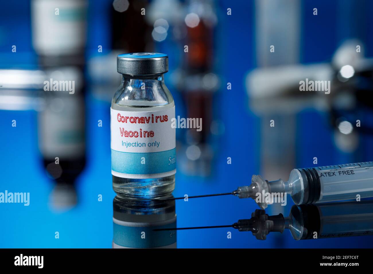 filet de verre de vaccin covid avec seringue et autres récipients de laboratoire placés sur une surface réfléchissante, isolés sur fond bleu Banque D'Images