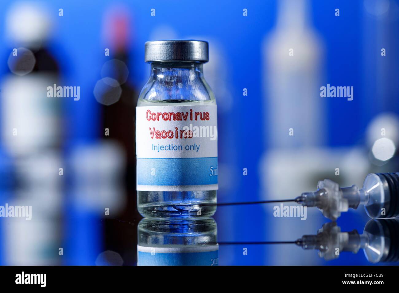 filet de verre de vaccin covid avec seringue et autres récipients de laboratoire placés sur une surface réfléchissante, isolés sur fond bleu Banque D'Images