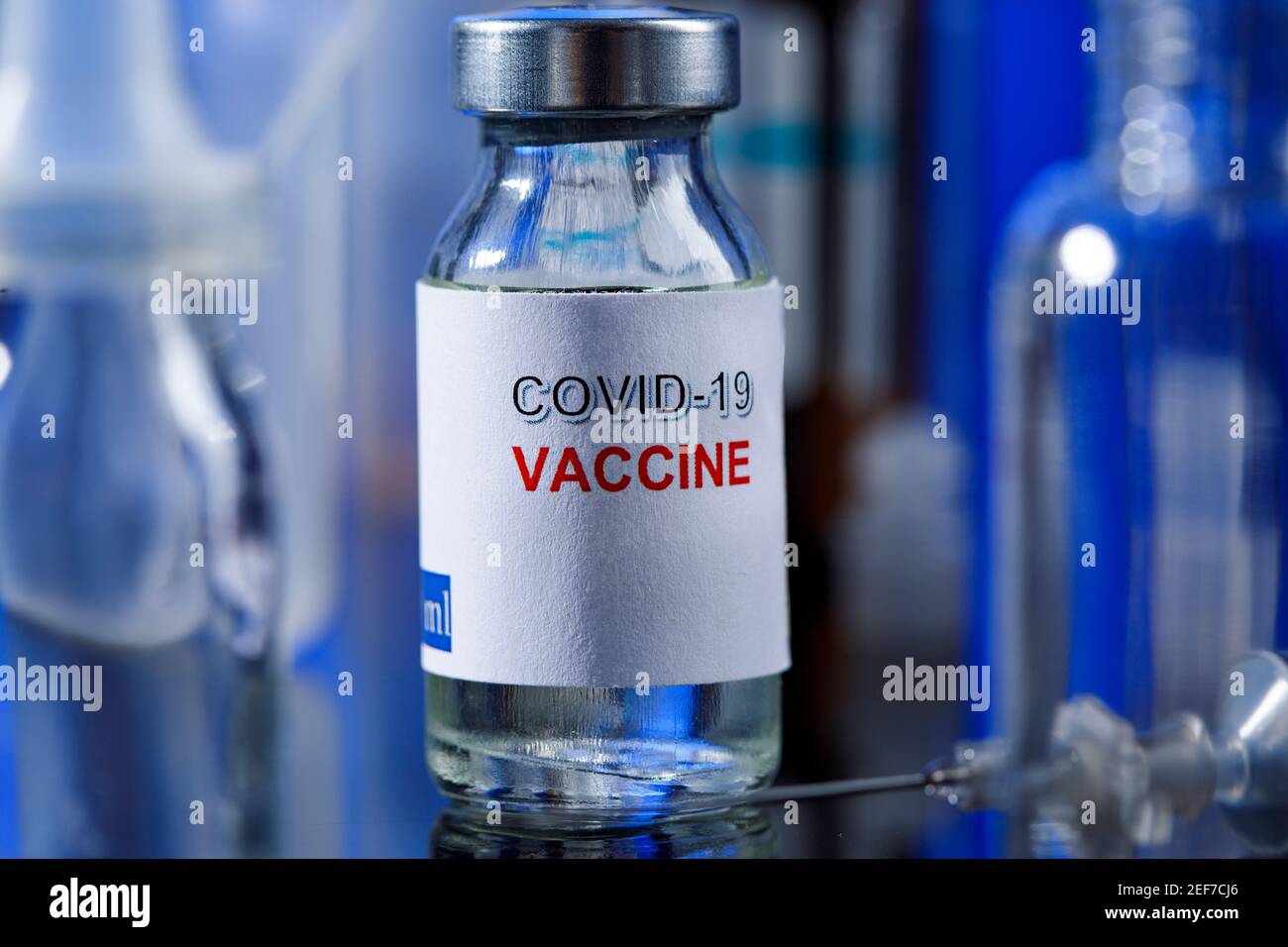 filet de verre de vaccin covid avec seringue et autres récipients de laboratoire placés sur une surface réfléchissante, isolés sur fond bleu Banque D'Images