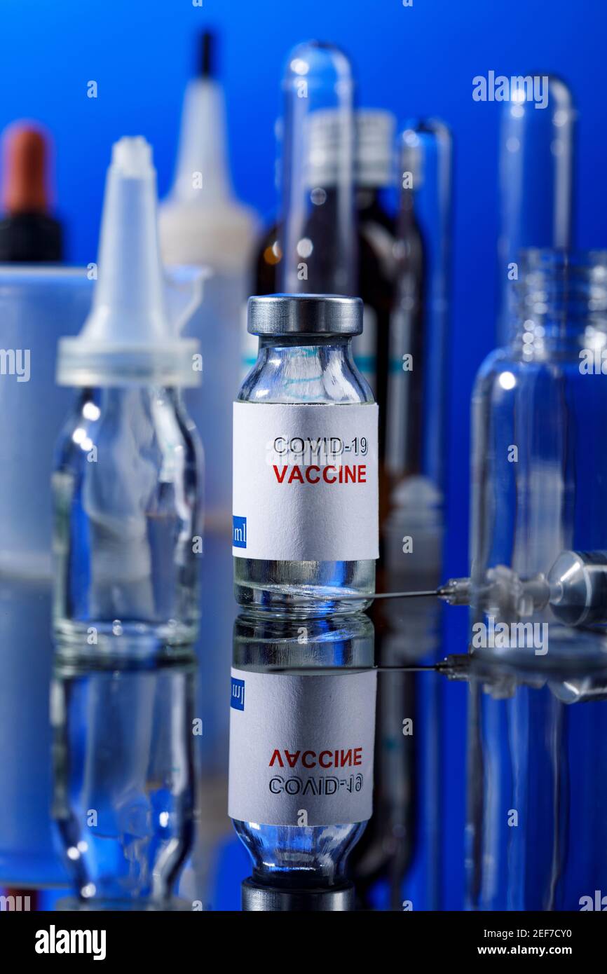 filet de verre de vaccin covid avec seringue et autres récipients de laboratoire placés sur une surface réfléchissante, isolés sur fond bleu Banque D'Images