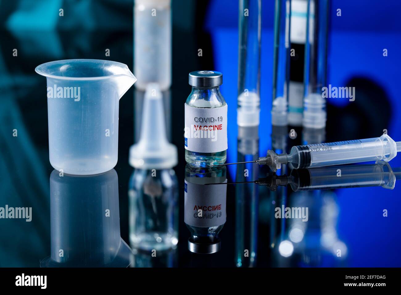 filet de verre de vaccin covid avec seringue et autres récipients de laboratoire placés sur une surface réfléchissante, isolés sur fond bleu Banque D'Images