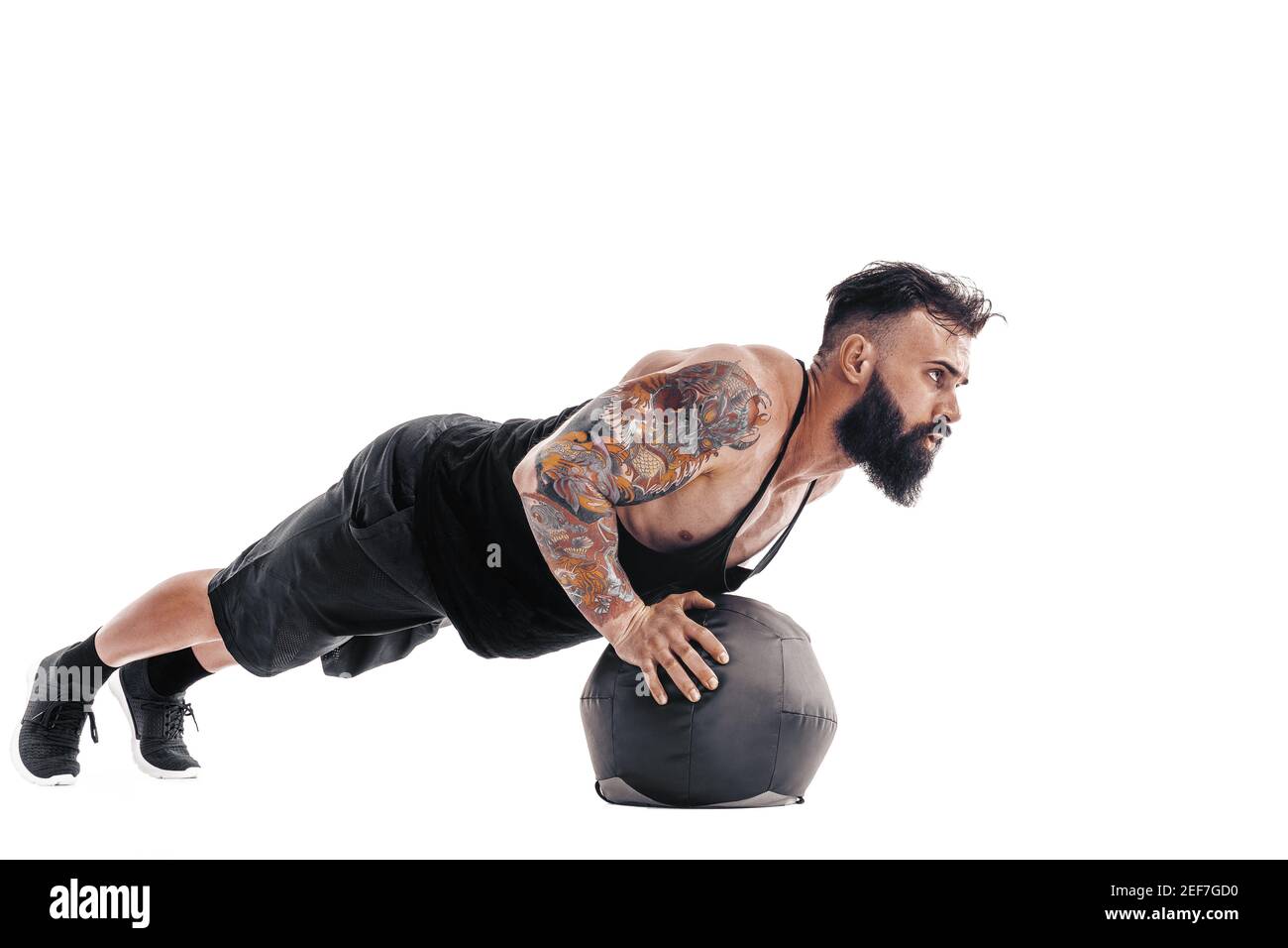 Musclé tatoué mâle barbu exercice poids de forme physique Medicine ball push-up exercices en studio isolé sur fond blanc. Banque D'Images