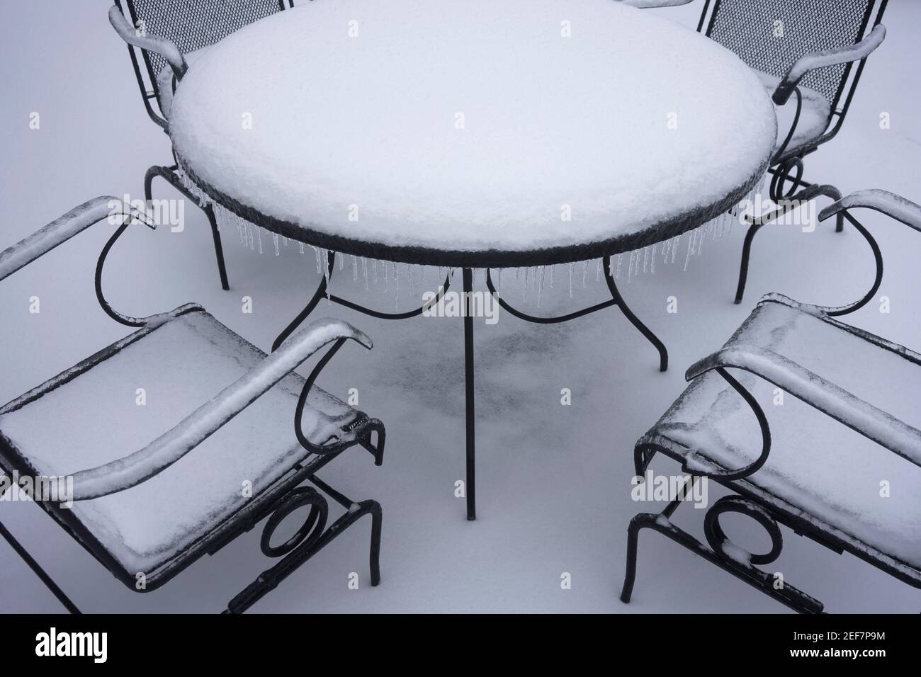 Une table et des chaises de patio extérieures surgelées et enneigées après la neige et la pluie verglaçante en hiver. Banque D'Images