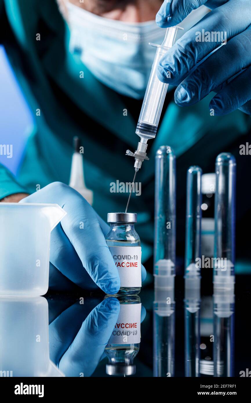 Médecin avec des capuchons médicaux et des gants en latex prend le vaccin covid avec une seringue dans un tableau avec plusieurs flacons Banque D'Images