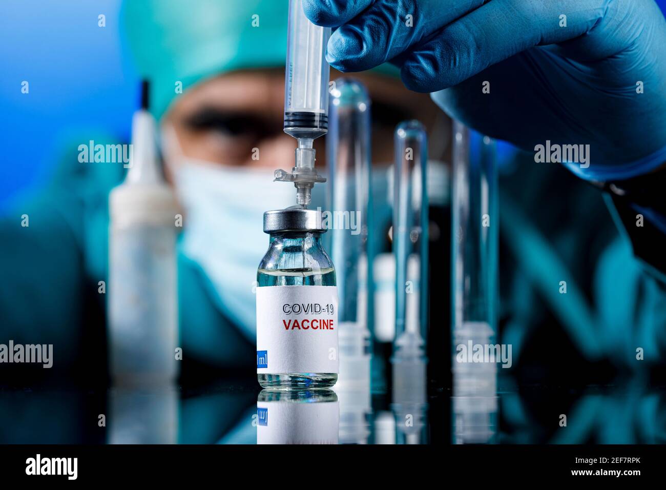 Médecin avec des capuchons médicaux et des gants en latex prend le vaccin covid avec une seringue dans un tableau avec plusieurs flacons Banque D'Images