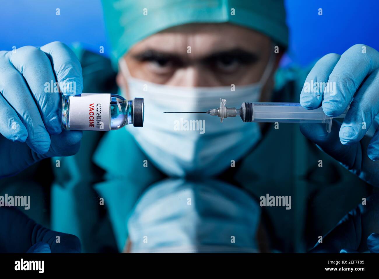 Médecin avec des capuchons médicaux et des gants en latex prend le vaccin covid avec une seringue dans un tableau avec plusieurs flacons Banque D'Images