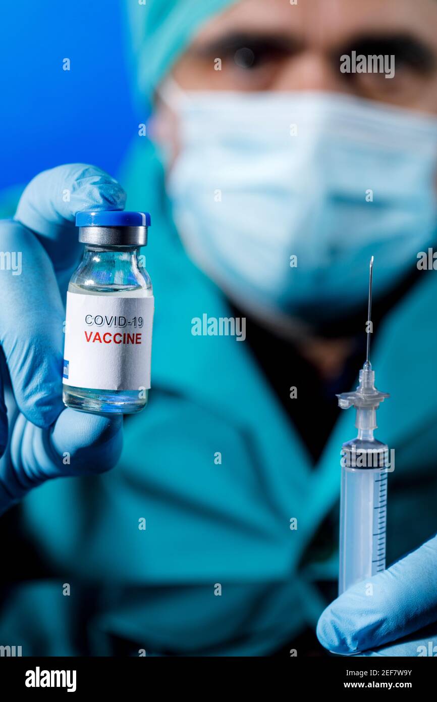 Médecin avec des capuchons médicaux et des gants en latex prend le vaccin covid avec une seringue dans un tableau avec plusieurs flacons Banque D'Images