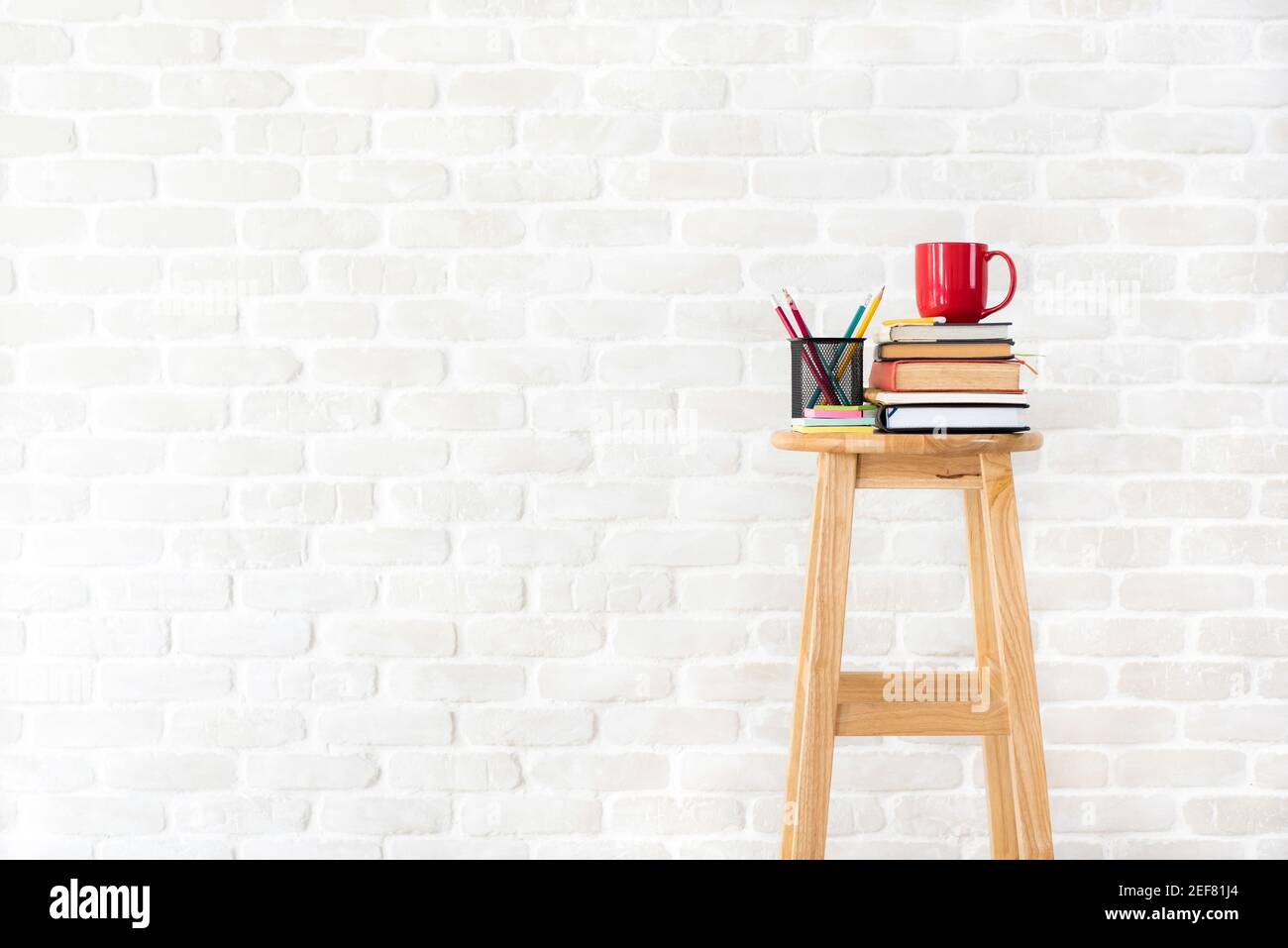 Livres, papeterie et tasse de café sur tabouret en bois dans fond de mur de brique blanche - idées, créatifs et concepts éducatifs Banque D'Images