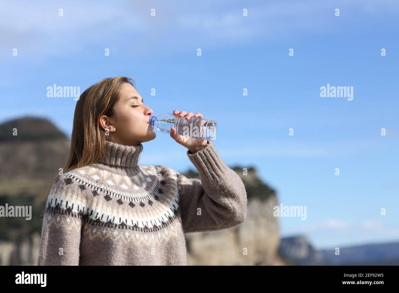 Vue latérale d'une femme buvant de l'eau en plastique bouteille en hiver dans la montagne Banque D'Images