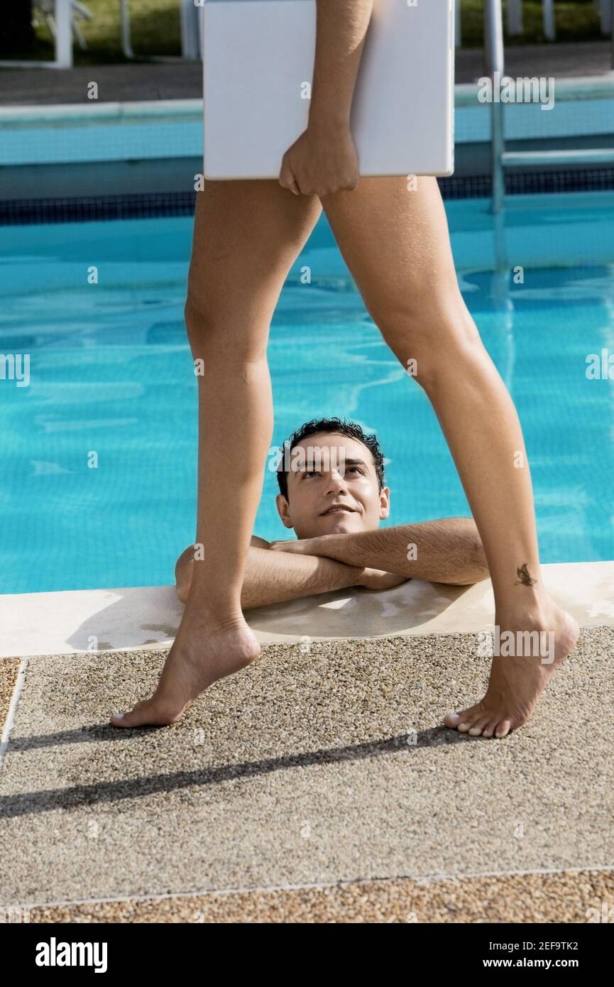 Vue en coupe basse d'une jeune femme portant un ordinateur portable avec un jeune homme la regardant dans une baignade piscine Banque D'Images
