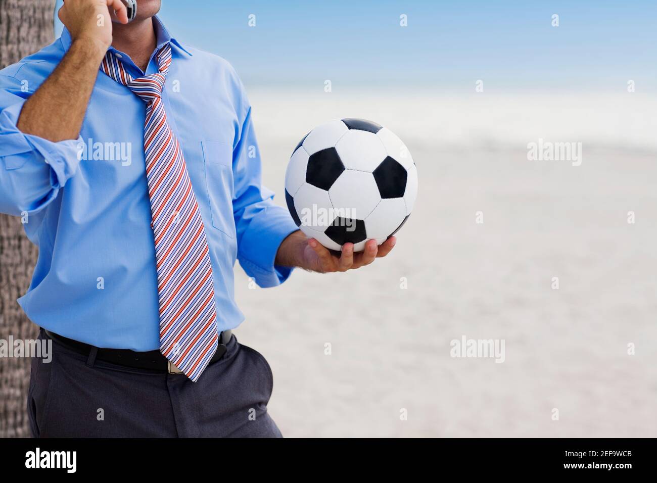 Vue en coupe centrale d'un homme tenant un ballon de football et parler sur un téléphone portable Banque D'Images