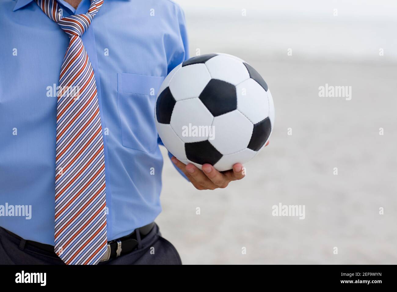 Vue en partie centrale d'un homme debout sur la plage et tenir un ballon de football Banque D'Images