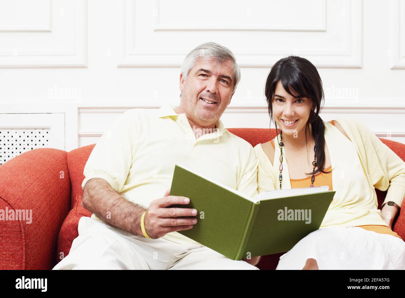Portrait d'un homme mûr assis avec sa fille un canapé et un livre Banque D'Images