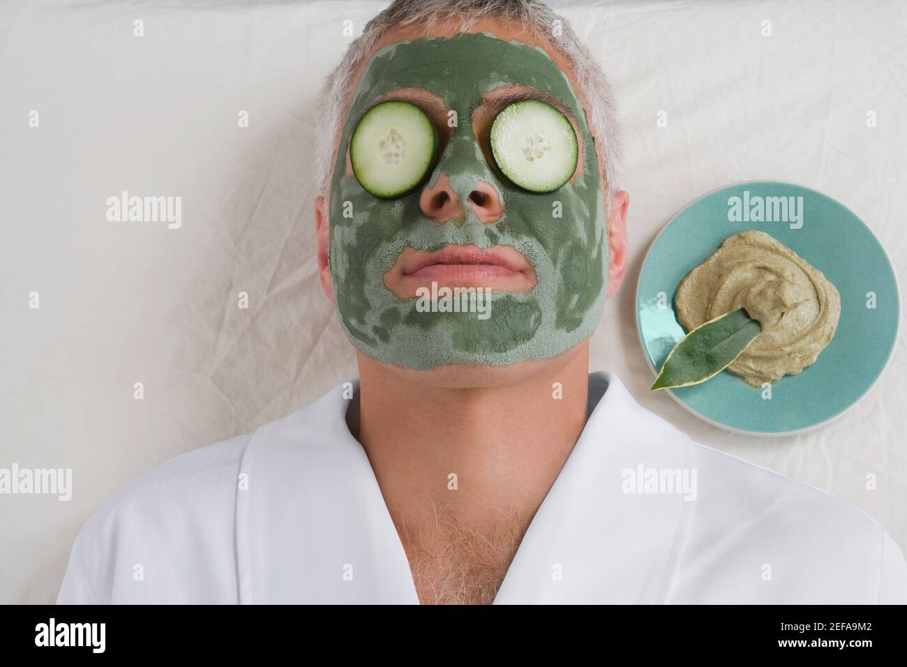 Gros plan d'un homme mûr allongé sur un visage empaqueter les tranches de concombre sur les yeux Banque D'Images