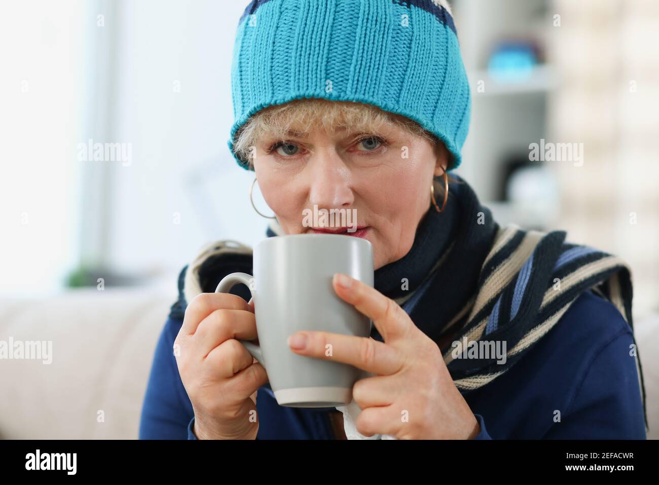 Portrait d'une femme âgée dans un chapeau chaud tenant une tasse avec des médicaments Banque D'Images