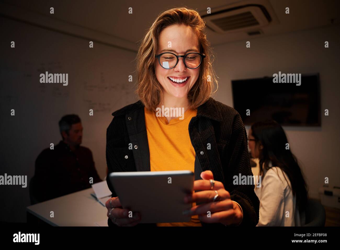 Portrait d'une jeune femme souriante à l'aide d'une tablette numérique et ses collègues travaillant en arrière-plan Banque D'Images