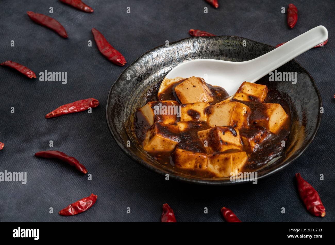 Matériel de la cuisine chinoise traditionnelle, le mapo tofu épicé décore avec des piments et des poivrons chauds sur fond noir. Banque D'Images