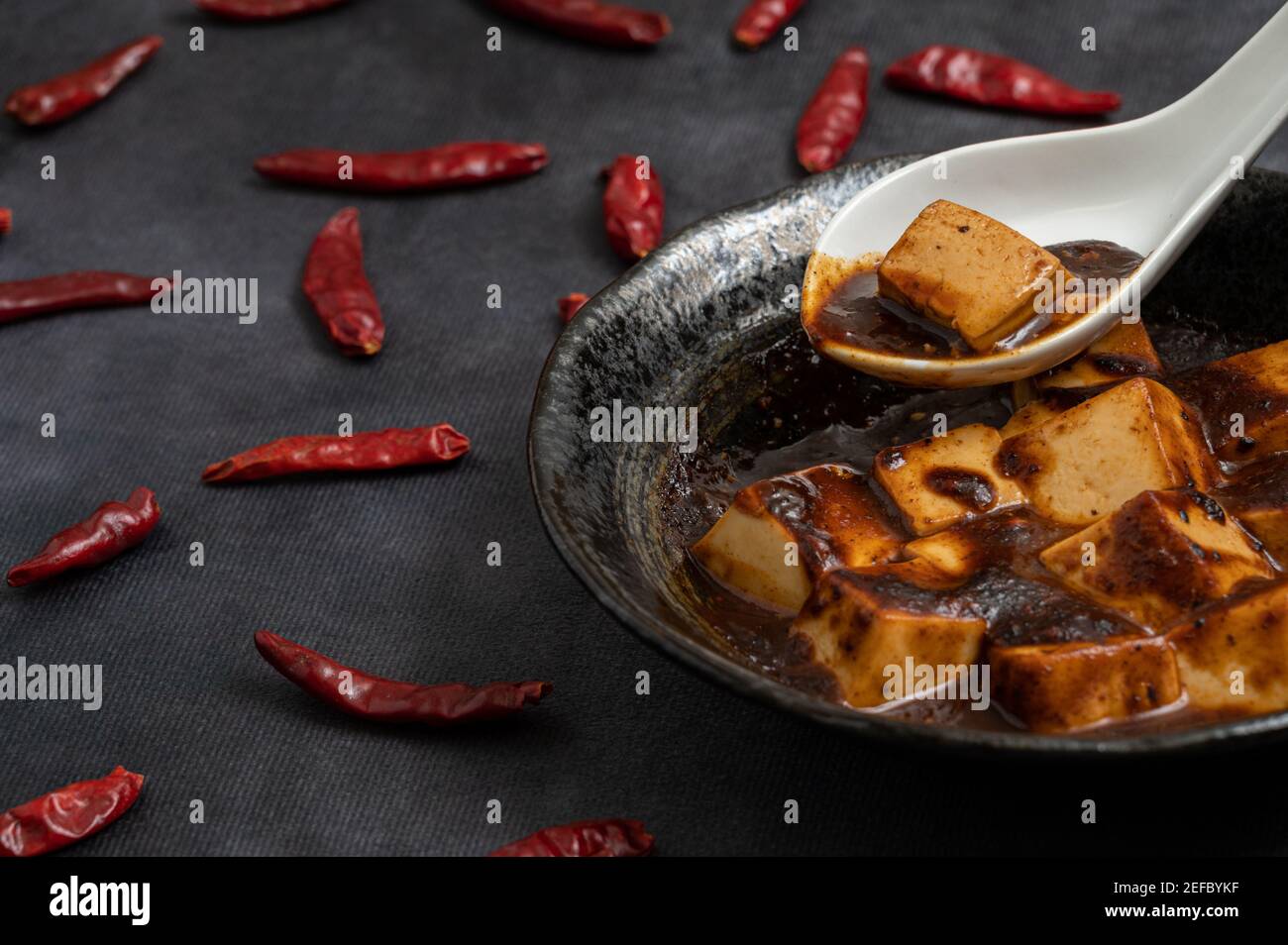 Matériel de la cuisine chinoise traditionnelle, le mapo tofu épicé décore avec des piments et des poivrons chauds sur fond noir. Banque D'Images