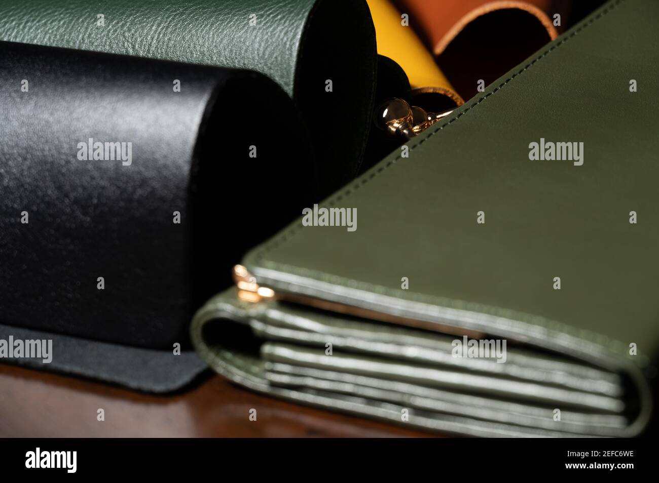 4 couleurs échantillon de cuir (noir, vert, jaune, marron) sur table en bois avec portefeuille vert avec fermoir métallique de couleur or. Matériaux pour l'industrie du cuir. Banque D'Images
