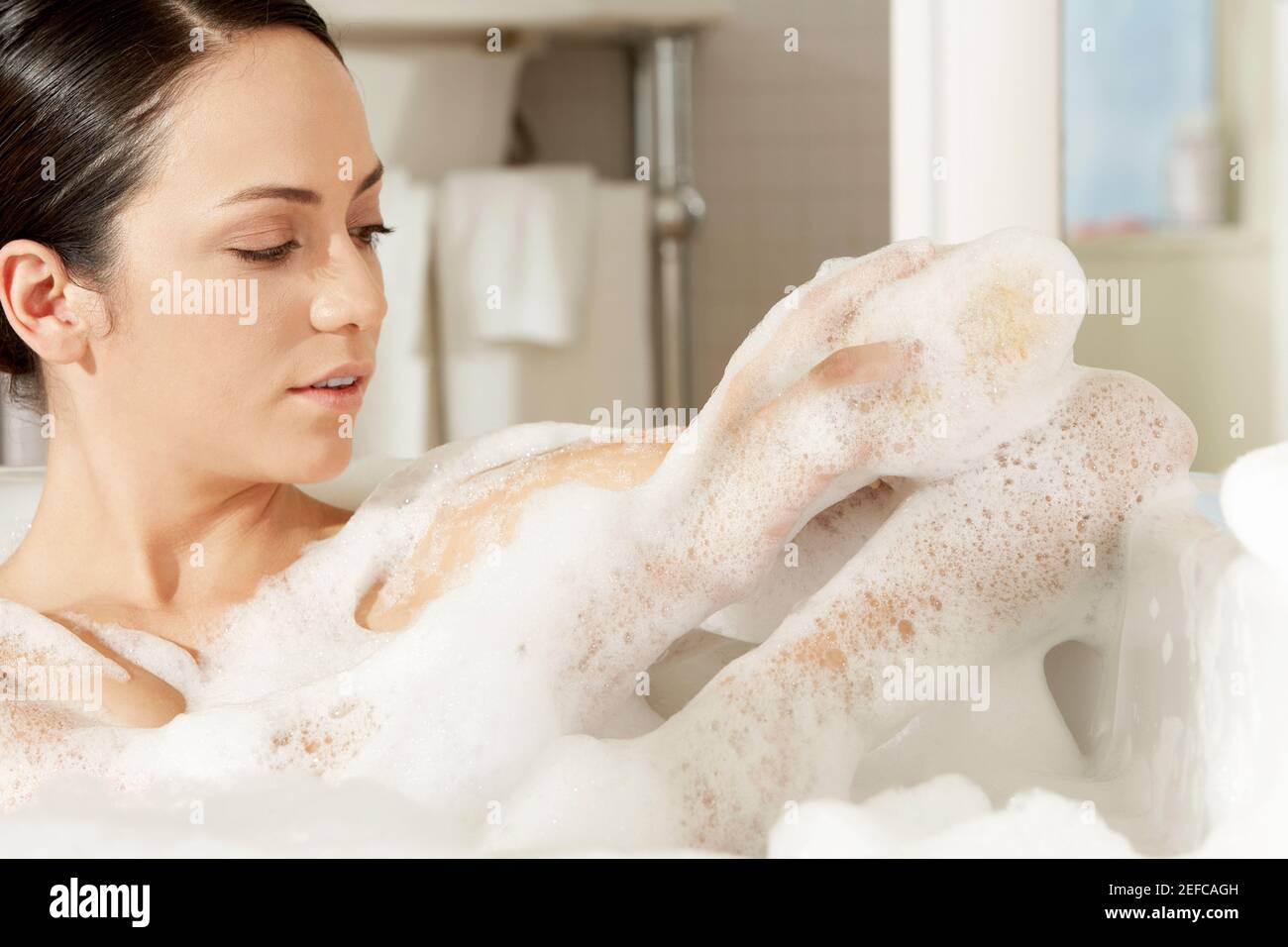 Gros plan d'une jeune femme utilisant une éponge de bain son bras Banque D'Images