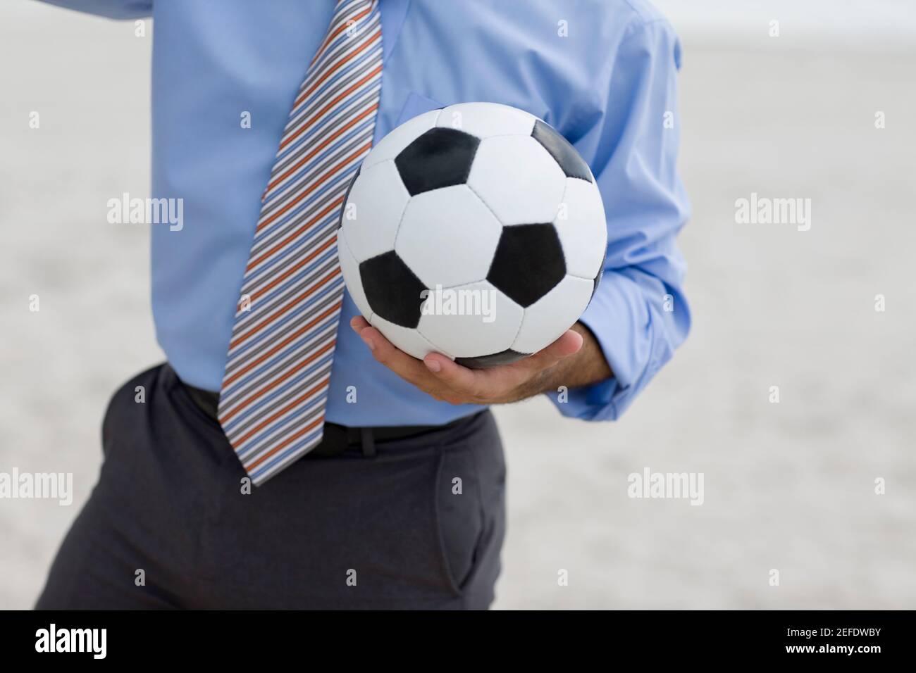 Vue en partie centrale d'un homme debout sur la plage et tenir un ballon de football Banque D'Images