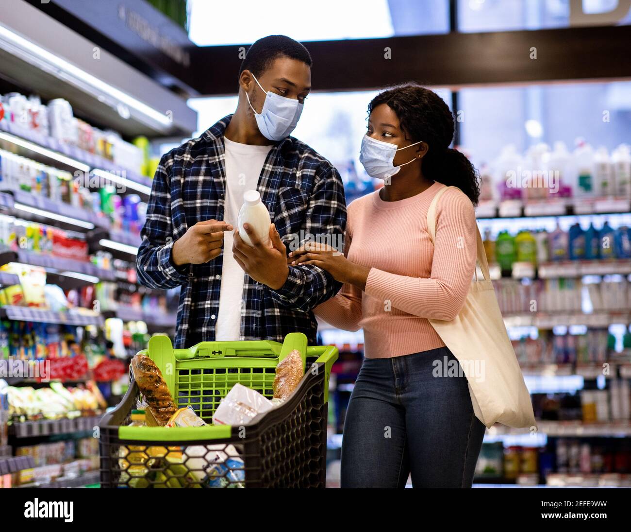 Jeune couple noir dans des masques protecteurs shopping pour la nourriture ensemble au supermarché pendant le verrouillage de covid. Femme afro-américaine millénaire et son petit garçon Banque D'Images