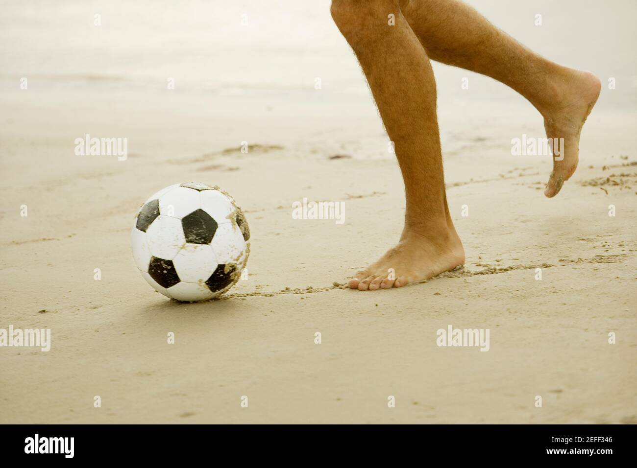 Vue en coupe basse d'un homme jouant au football sur le plage Banque D'Images