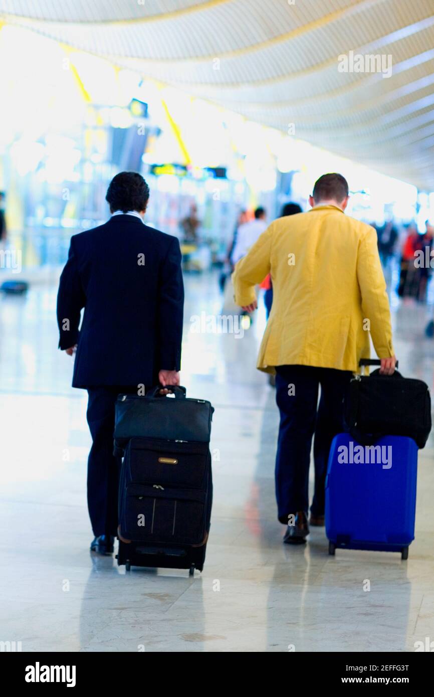 Vue arrière de deux hommes marchant et tirant des bagages à un aéroport, Madrid, Espagne Banque D'Images